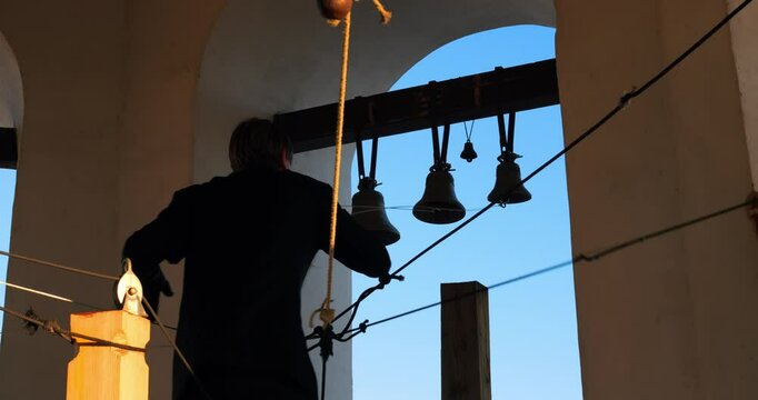Bell ringer skillfully pulling ropes high up in majestic tower during beautiful sunset evokes deep faith and rich history with strikingly silhouetted bells against vibrant sky. Orthodoxy concept