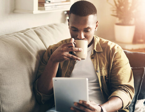 House, coffee and black man on sofa, tablet and reading morning news, relax and internet. African person, apartment and guy on couch, technology or herbal tea with digital app for ebook or connection