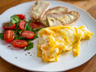 Continental breakfast - scrambled eggs, slice of bread with butter  and fresh vegetables on wooden table
