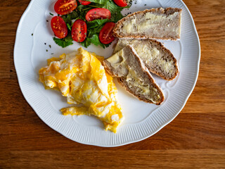 Continental breakfast - scrambled eggs, slice of bread with butter  and fresh vegetables on wooden table
