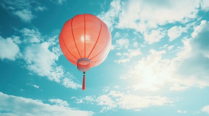 Obraz premium A single red Chinese lantern floats in a bright blue sky with white clouds, symbolizing hope and good fortune.