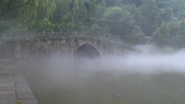 Ancient stone bridge shrouded in mist in the Wudang Mountains, China. The ethereal fog adds a mystical touch to this serene landscape, enhancing its timeless, tranquil beauty.