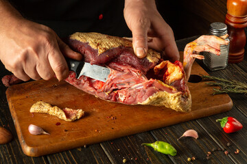 A chef expertly carves a rich piece of meat, revealing tender textures. The warm kitchen is adorned with fresh herbs, spices, and vibrant vegetables, inviting culinary creativity