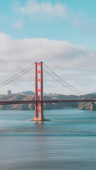 Obraz premium Golden Gate Bridge spans tranquil waters, framed by hills and a skyline Vertical Mobile Wallpaper
