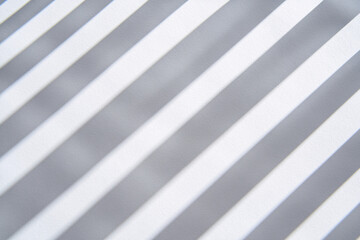 Obraz premium Blurred pattern of window blind shadows forming abstract symmetrical lines on a white surface 