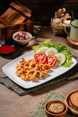 Crispy fried squid on a white plate with tomatoes, cucumber and lettuce