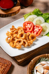 Crispy fried squid on a white plate with tomatoes, cucumber and lettuce