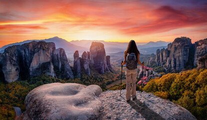 A hiker woman stands on a rock and looks at a beautiful sunset beahind the Meteora valley mountains, Kalabaka, Greece © moofushi