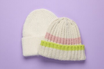 Warm woolen hats on lilac background, top view
