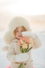 Little girl in a winter forest holding tulips