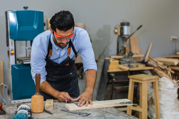 Young carpenter man Check quality and size for making wooden furniture in factory. Male working in wooden industry joiner workshop. Craftsman professional concept.
