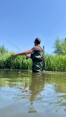Fototapeta premium Fisherman casting line in a river on a clear summer day
