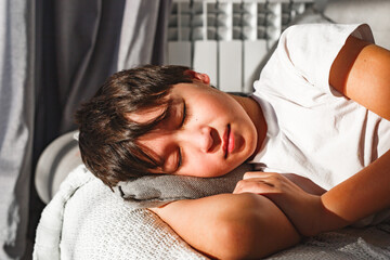 Cute tired boy sleeping in comfortable  sofa in beams of morning sun © Olga Gimaeva