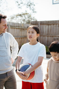 Pre-teen girl holding a ball outdoors with her dad and brother