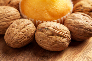 Fresh baked muffin surrounded by raw whole organic walnuts on a wooden surface, showcasing a natural wholesome snack. Close up 
