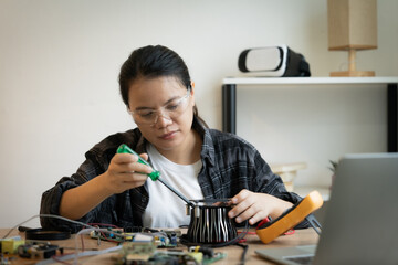 A woman is working on a computer part. She is wearing a white shirt and a black plaid shirt