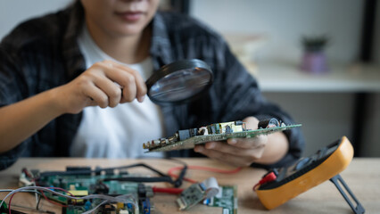 A woman is looking at a small electronic device with a magnifying glass. She is examining the device to see if it is working properly