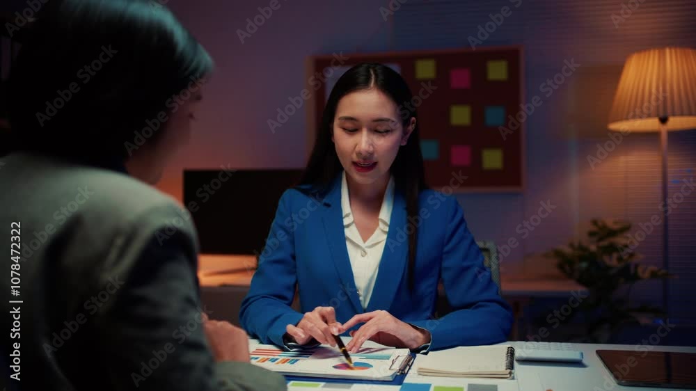 Poster businesswoman pointing at charts while explaining details to her partner. both are seated at a desk 