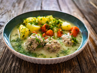 Boiled meatballs in dill sauce with potatoes and vegetables on wooden table
