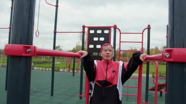 A woman in a red beanie and sporty jacket exercises on parallel bars in an outdoor fitness park. She performs dips with focus and determination, promoting an active and healthy lifestyle.