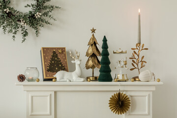Elegant Christmas mantel decor with gold and green accents, festive trees, and a reindeer figurine. Sophisticated holiday style.