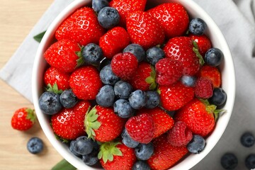 Different fresh ripe berries in bowl on wooden table, top view