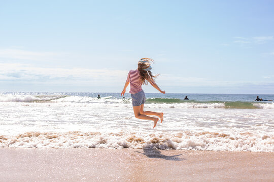 ten year old girl jumping over breaking waves at the beach
