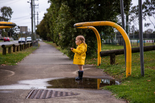 toddler girl in a yellow raincoat standing in a puddle on a path