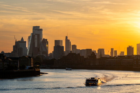 A picturesque view of a city skyline at sunset, capturing the serene beauty of a river with boats gently moving along, reflecting the evening's golden hues in London UK
