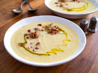 White vegetable cream soup served with walnuts and olive oil on wooden table
