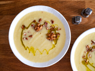 White vegetable cream soup served with walnuts and olive oil on wooden table
