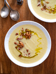 White vegetable cream soup served with walnuts and olive oil on wooden table
