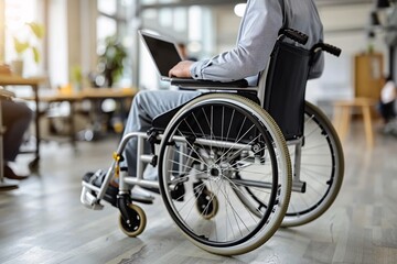 Obraz premium A person sits in a wheelchair, focused on a laptop, in a contemporary office environment filled with natural light. The setting is warm and inviting, promoting productivity
