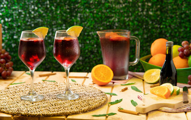Two glasses of handmade summer wine next to decanter, oranges, lemons and bottle of wine on rustic wooden table