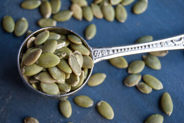 Green pumpkin seeds in a silver spoon on a blue background, emphasizing natural textures.