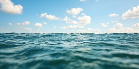 Obraz premium A serene view of calm ocean waters under a clear blue sky with fluffy clouds.