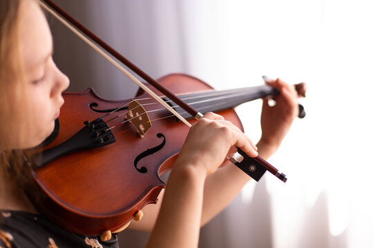 child playing a violin in front of a window