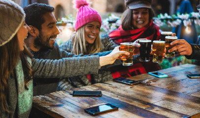 Young friends having fun together drinking craft beers at pub restaurant - Winter lifestyle and party concept - Soft focus on left man