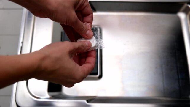 A hand taking out dishwasher filter to clean it, dis washer cleaning concept, kitchen home appliances care and maintenance