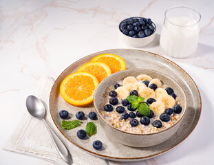 Steel cut oats soaked overnight topped with banana, blueberries, and slices of orange on the side served with almond milk; plant-based diet; copy space