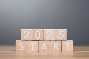 Businessman arranges wooden blocks spelling out 'START 2025' on a table, symbolizing the beginning...