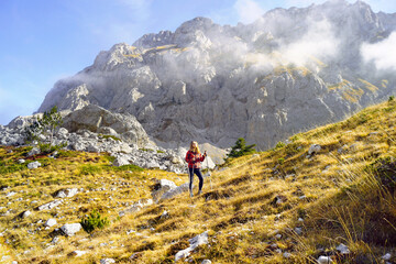 Fototapeta premium Travel to the east of Montenegro: a woman in a red checkered jacket photographed from afar stands in the Medjukomlje valley. A female tourist in front of a stunning view in the Komovi mountains