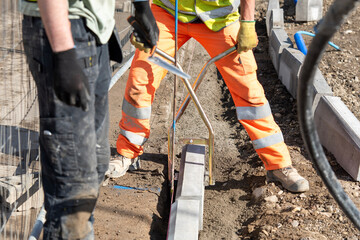 Construction workers placing concrete kerb on concrete for sidewalk 