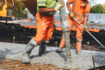 Construction workers pouring concrete on a job site in bright orange uniforms during daylight hours
