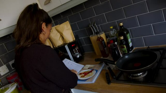 Cute young couple cooking together looking at a cook book and prepping ingredients