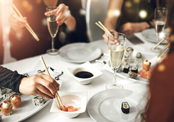 Hands, friends and sushi in restaurant for lunch, social gathering and sharing at table. People, Japanese cuisine and champagne for fine dining with luxury food, birthday celebration or girls bonding