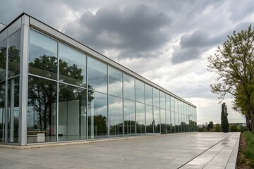 Obraz premium Stunning Minimalist Architecture featuring a Modern Building with a Large Glass Facade Reflecting the Sky and Surrounding Nature in an Urban Environment