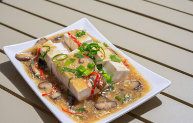 Stir-fried tofu or RAD na  tofu  with Chicken eggs, slide  spring onions, mushrooms and red chili peppers. Healthy vegetarian food on a white plate.