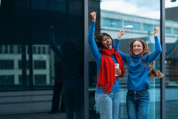 Obraz premium Two young women celebrate joyfully outdoors in urban setting while enjoying leisure time together during the day