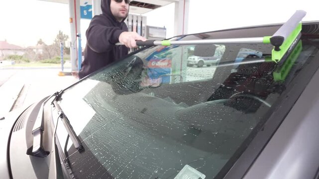 Person cleaning sports car windshield on blue gas station